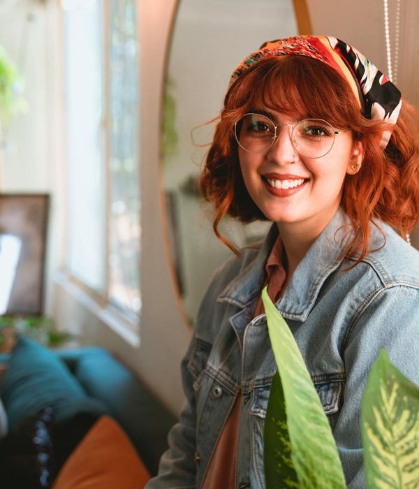 Woman smiling peacefully in a bright, airy room with plants.